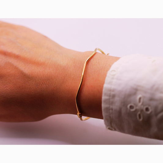 Golvende bangle 2 mm 14k goud, gedragen om de pols bij een witte mouw
