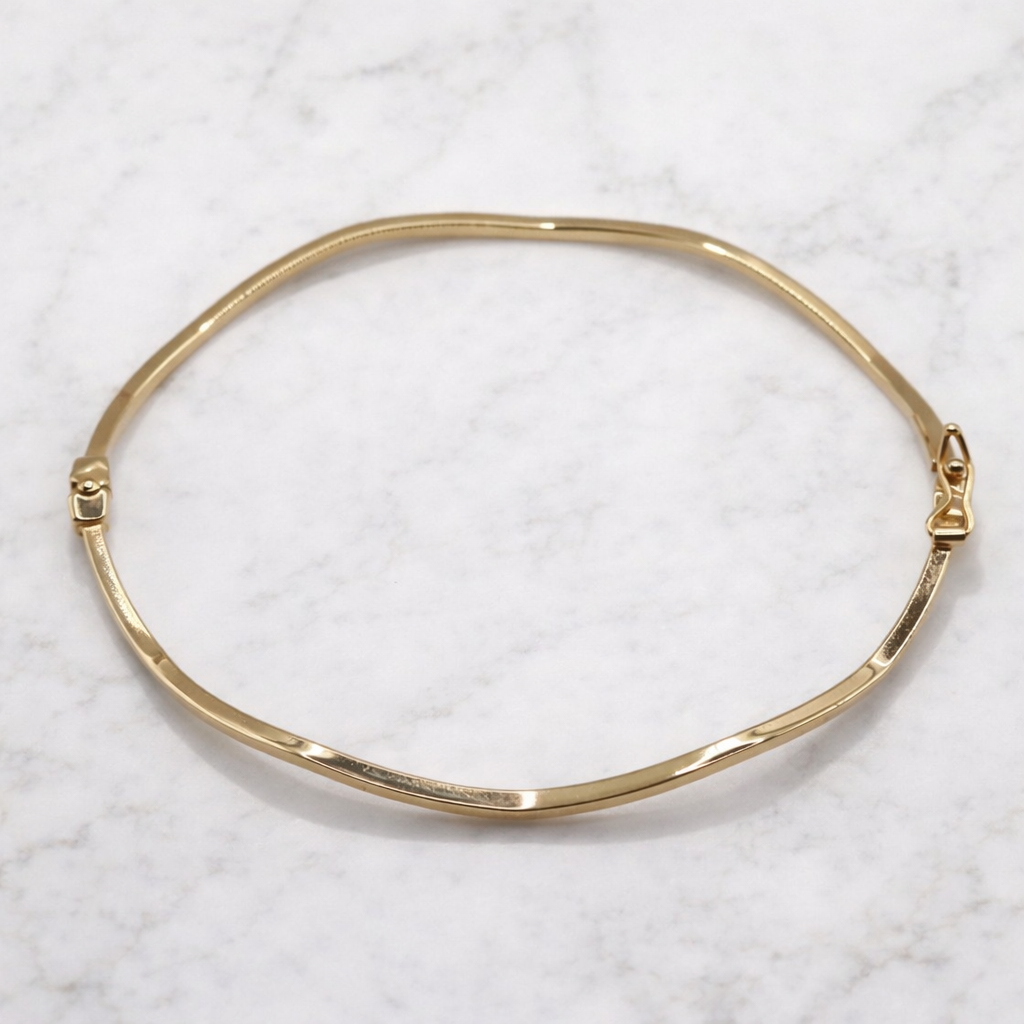 Golvende bangle hoekige vorm 14k goud, bovenaanzicht op marmer
