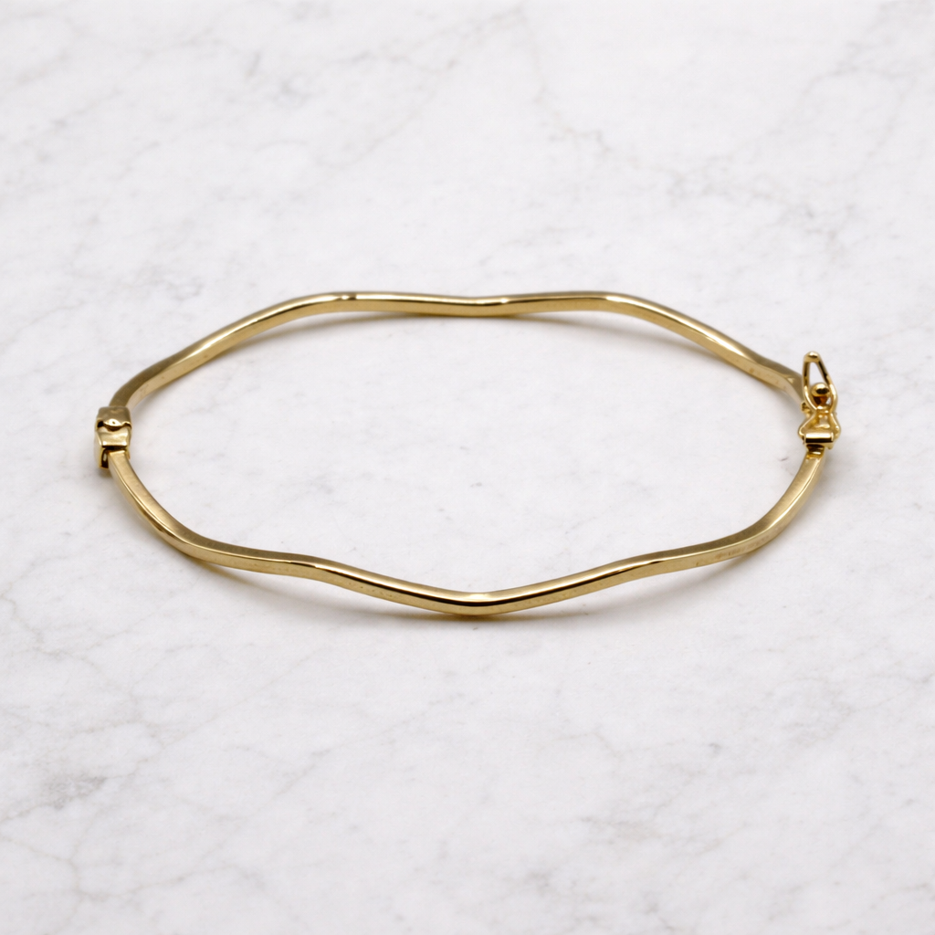 Golvende bangle hoekige vorm 14k goud, schuin op marmer met zichtbare golfvorm