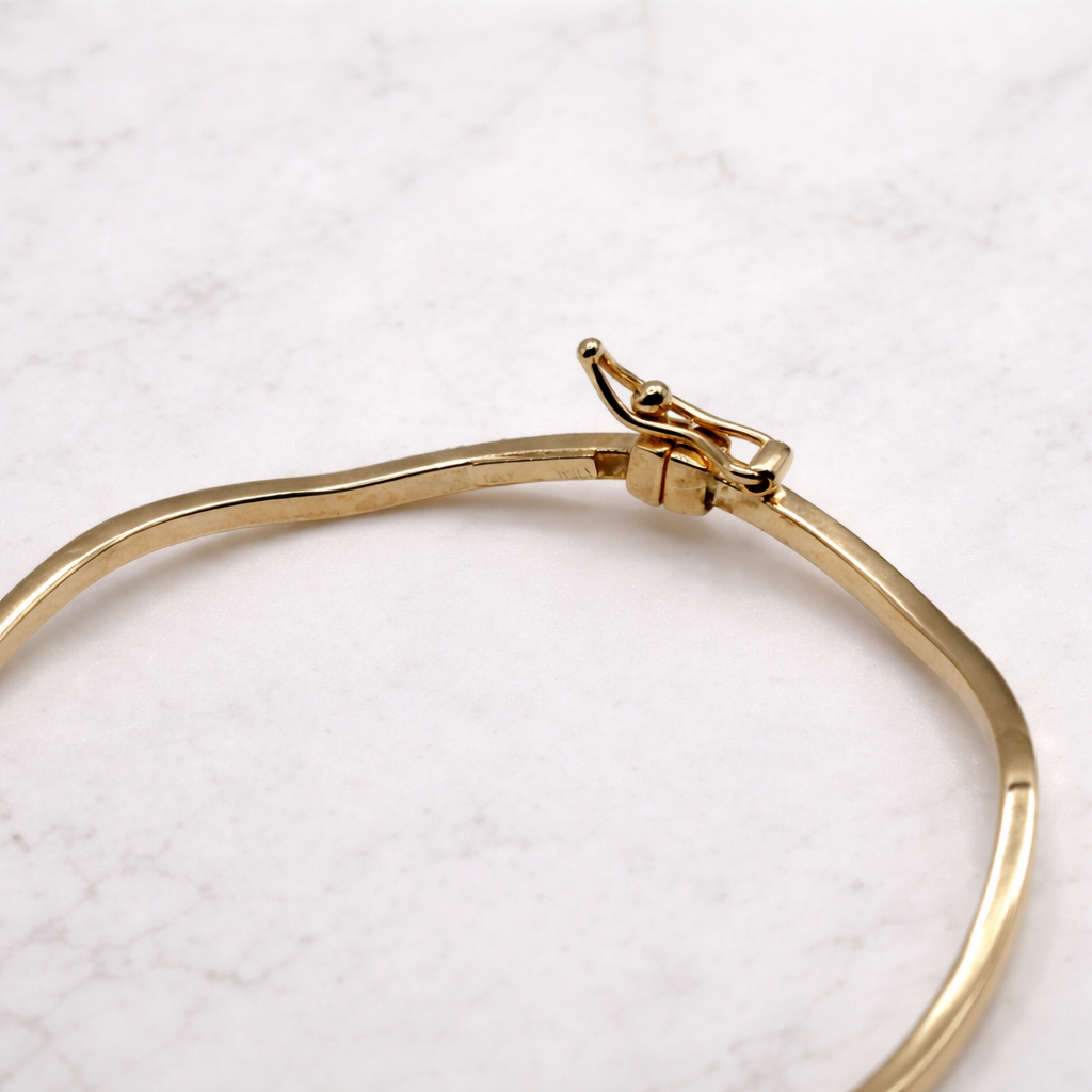 Golvende bangle hoekige vorm 14k goud, close-up van de open klapsluiting op marmer
