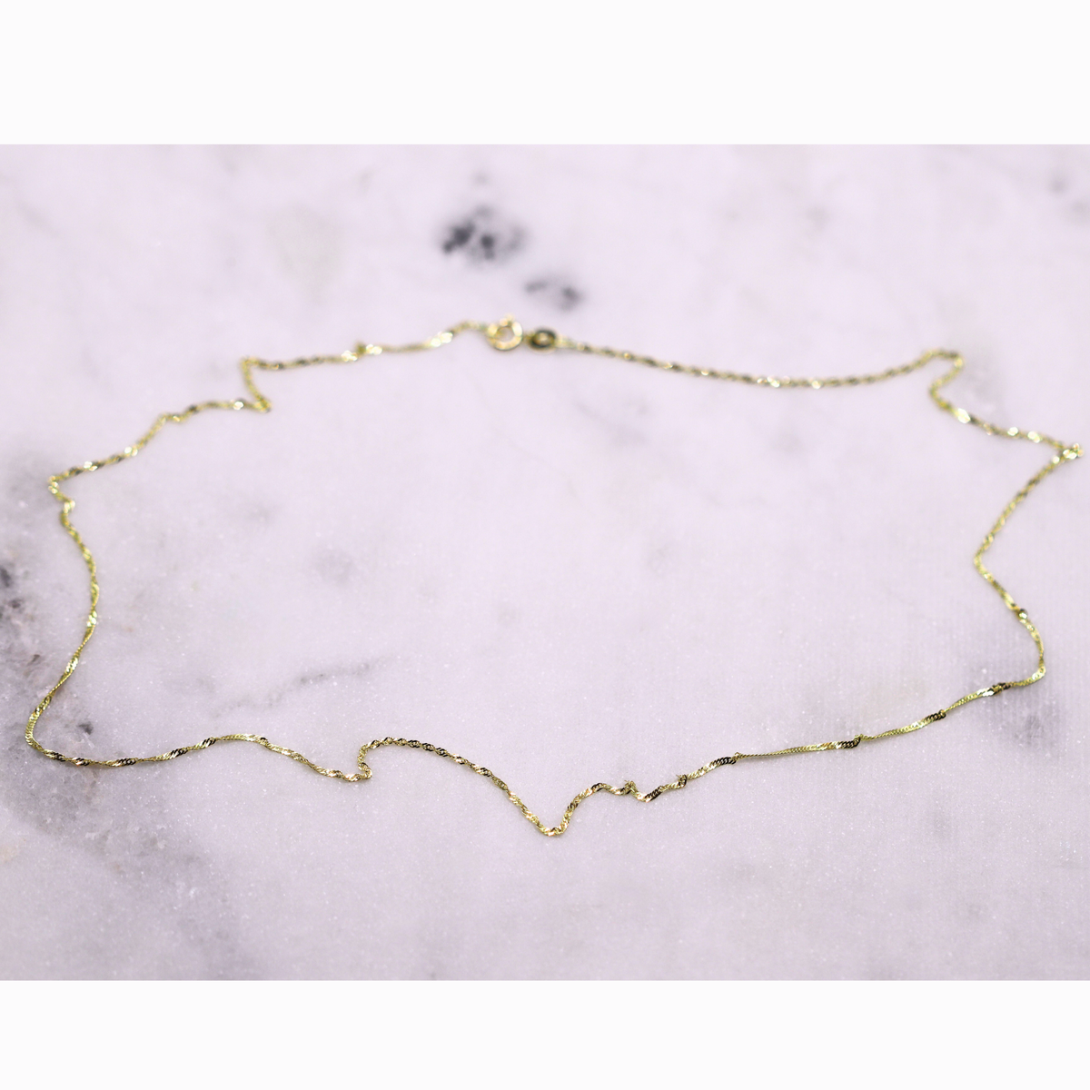 Singapore Ketting 1 mm 14k goud, opengelegd op natuursteen