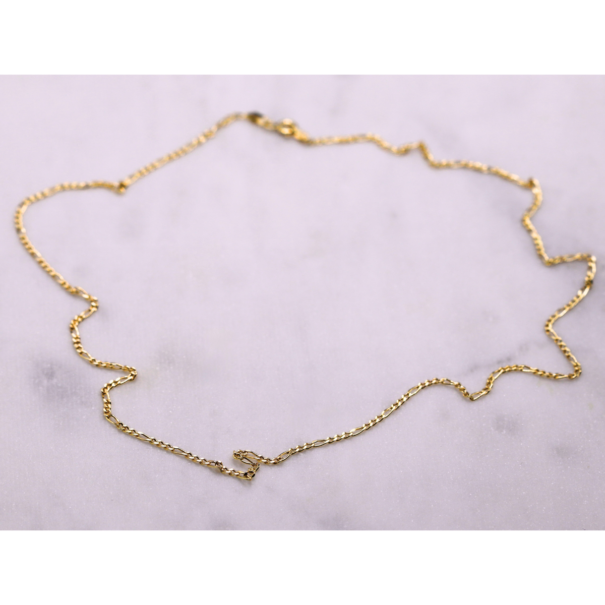Figaro schakelketting 2 mm 14k goud, opengelegd op natuursteen