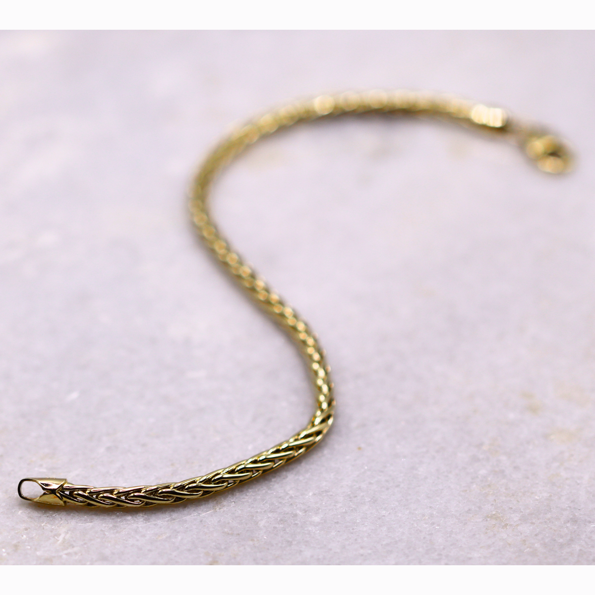 Gevlochten Vossenstaart armband 3 mm 14k goud, S-vormig opengelegd op natuursteen