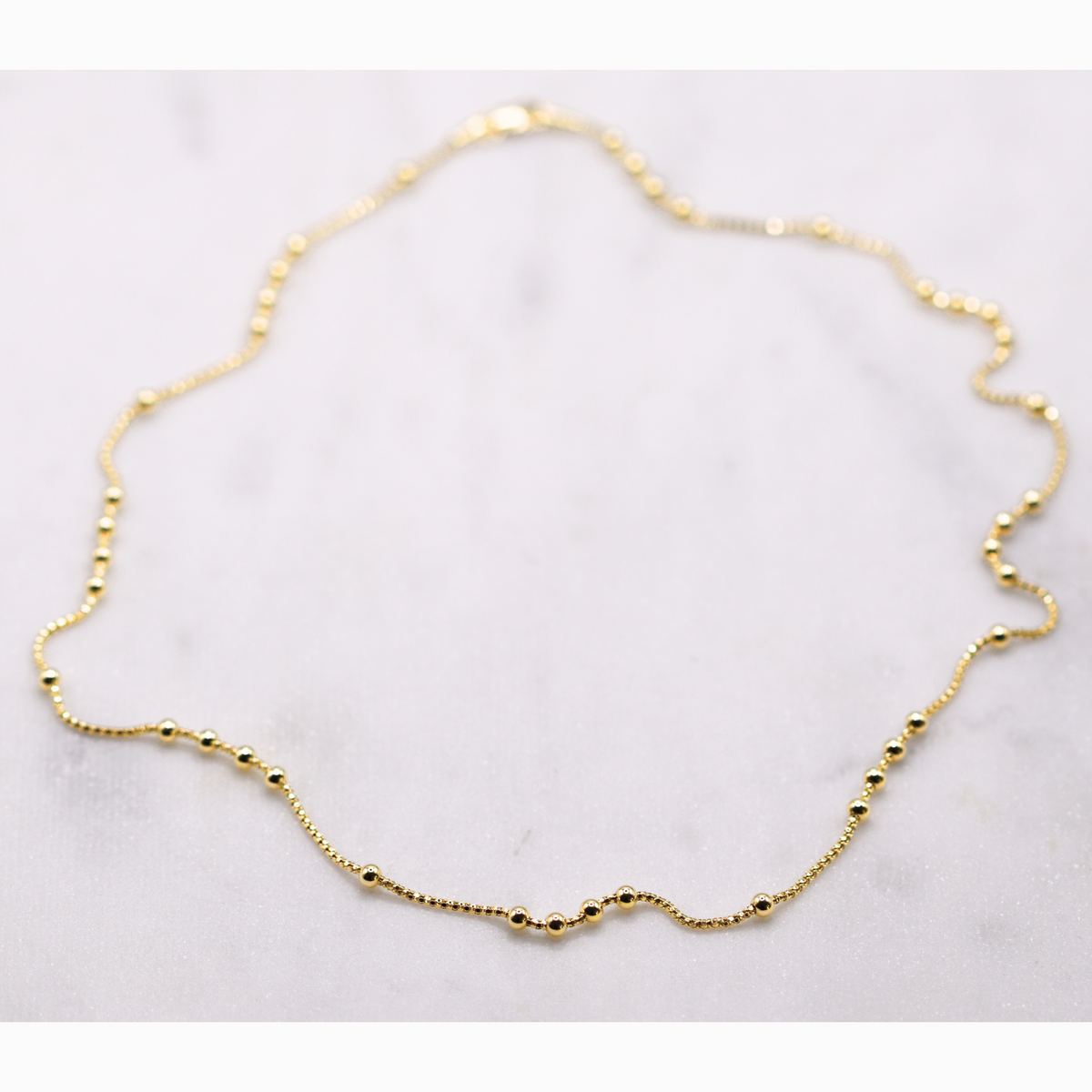 Bolletjes station ketting 3 mm 14k goud, opengelegd op natuursteen