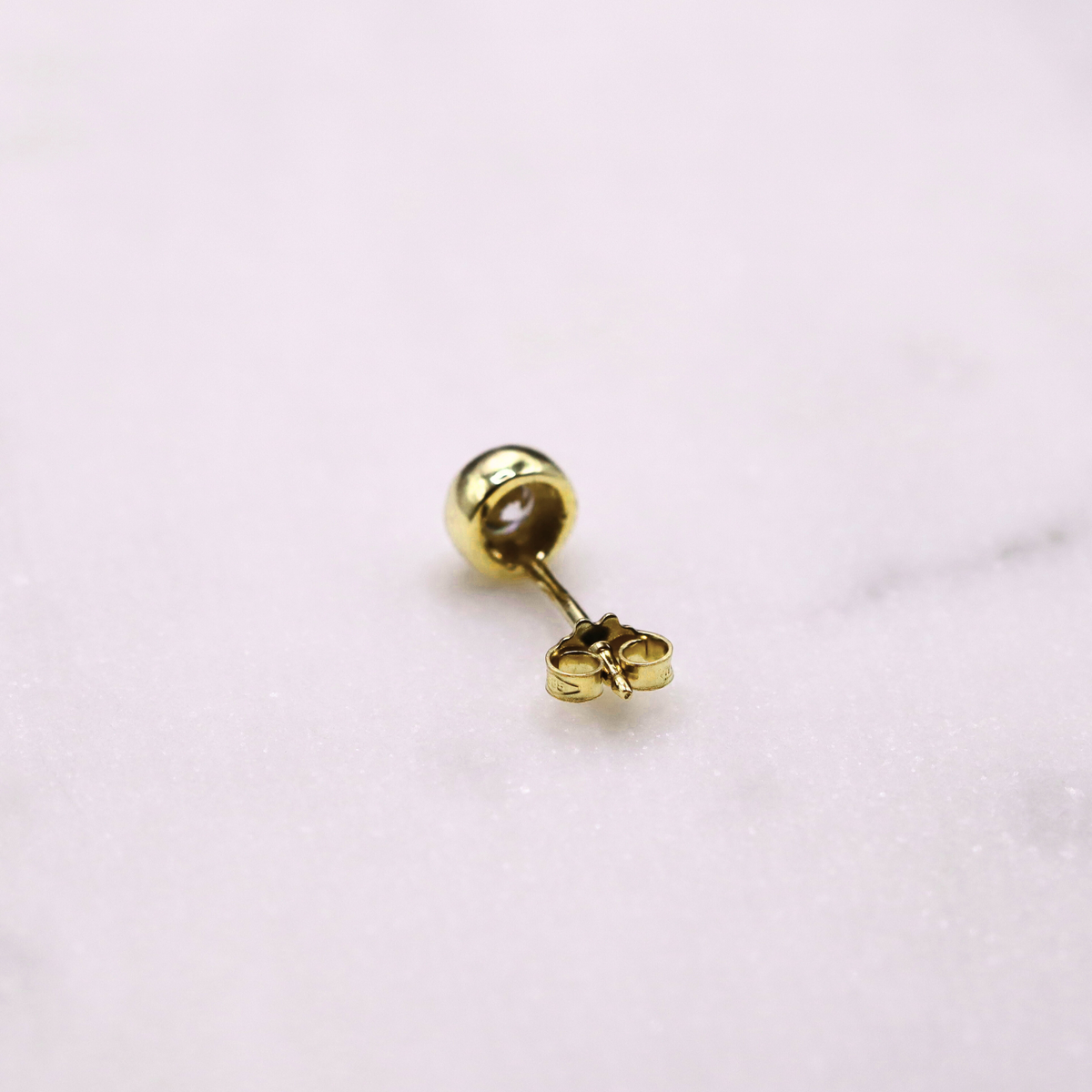 Bezel oorstekers zirkonia 14k goud, close-up op natuursteen